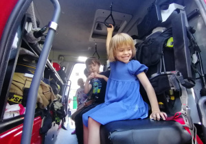Dzieci siedzą w wozie strażackim.
