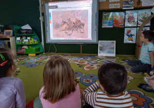 Dzieci oglądają dzieła malarstwa o tematyce zimowej, na tablicy multimedialnej.