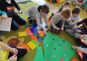 Dzieci drą papier kolorowy na mniejsze fragmenty, robiąc płatki kwiatka.