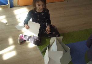 Dziewczynka buduje domek z papieru.