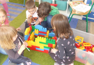 Dzieci budują domek z klocków plastikowych.