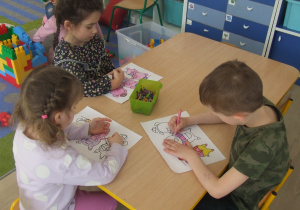Dzieci kolorują ilustrację trzech świnek.