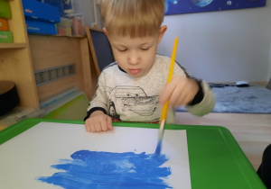 Chłopiec maluję farbami kartkę.