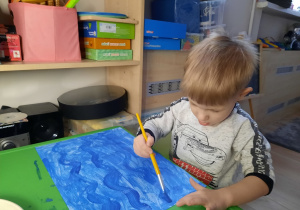 Chłopiec maluje fale na kartce.