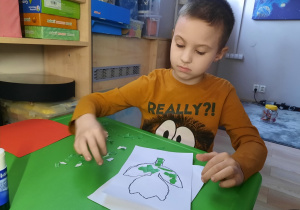 Chłopiec przykleja fragmenty papieru kolorowego na kwiatku.