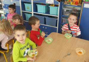 Dzieci jedzą przy stolikach słodkie jajeczka.