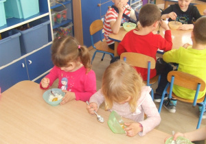 Dzieci jedzą przy stolikach słodkie jajeczka.
