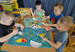 Dzieci malują farbami talerzyki papierowe.