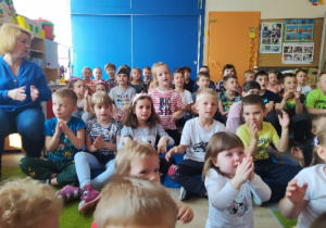 Dzieci siedzą na widowni i śpiewają piosenkę.