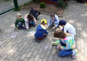Dzieci malują kredą na kostce brukowej.