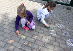 Dzieci malują kredą na kostce brukowej.