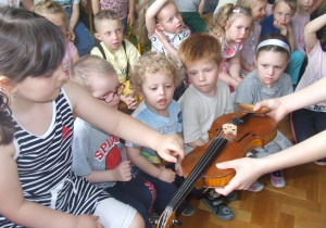 Dzieci szarpią struny skrzypiec.
