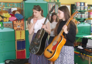 Studentki pokazują rożne rodzaje gitar.