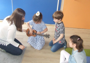 Dziewczynka próbuje grać na ukulele.