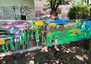 Dziewczynka maluje na streczu farbami kwiaty.