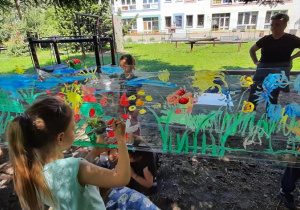Dzieci maluja farbami na streczu łąkę.