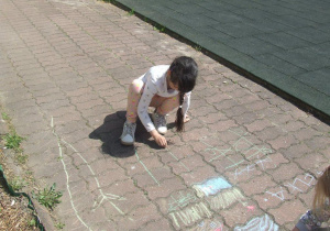 Dziewczynka rysuje kredą na chodniku.