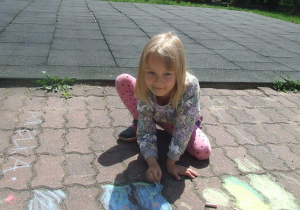 Dziewczynka rysuje kredą na chodniku.
