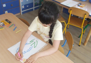 Dziewczynka rysuje kredkami po folii po śladzie kwiatka.
