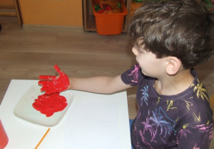Chłopiec odciska swoja dłoń w farbie.