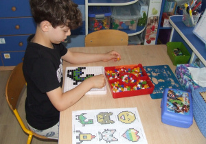 Chłopiec układa mozaikę geometryczną wg wzoru.