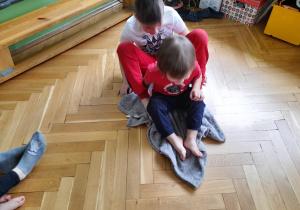 Chłopcy przesuwają się na kocu po podłodze.
