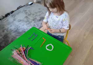 Dziewczynka układa litery z drucików kreatywnych.