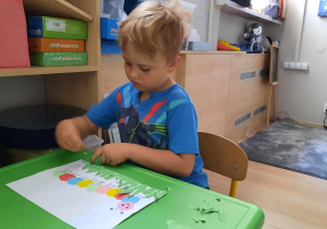 Chłopiec przykleja kawałki zielonego papieru do kartki.