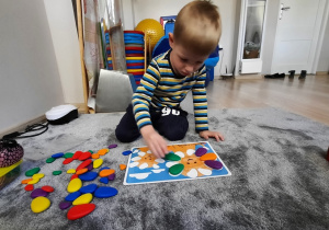 Chłopiec nakłada kolorowe elementy na szablon.