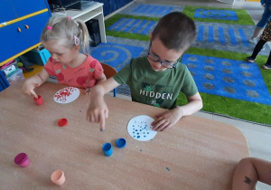 Dzieci na białym kółku robią kropki z farby.