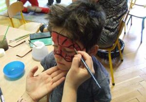 Nauczycielka maluje twarz chłopca.