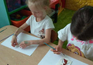 Dziewczynki malują obrazek z gliny.