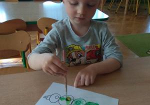 Chłopiec maluje farbami obrazek.