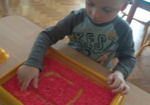 Chłopiec rysuje kształty na tacy z piaskiem.