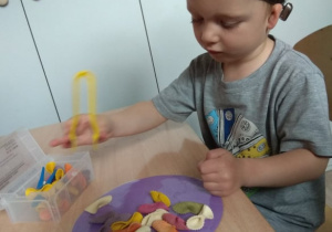 Chłopiec przenosi szczypcami makaron.