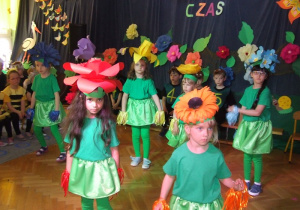 Dziewczynki w przebraniu kwiatów tańczą na scenie.