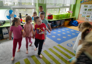 Dzieci spacerują po dywanie trójkami.