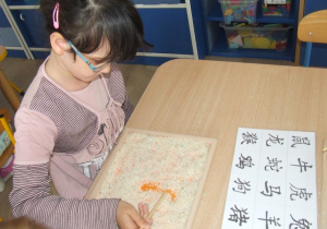 Dziewczynka rysuje chińskie znaki pałeczkami.