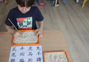 Chłopiec rysuje chińskie znaki pałeczkami.