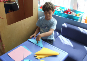 Chłopiec składa origami z kwadratów.