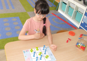 Dziewczynka z użyciem klocków z przyssawkami gra w kółko i krzyżyk.
