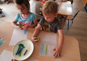 Dzieci kolorują kartkę kredkami w kolorze niebieskim i zielonym.