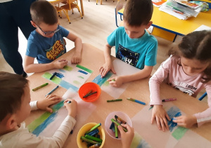 Dzieci kolorują kartkę kredkami w kolorze niebieskim i zielonym.