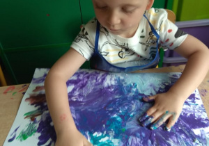 Chłopiec maluje farbami.