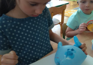 Dziewczynka stempluje kartkę balonem z farbą.