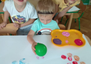 Chłopiec stempluje kartkę balonem z farbą.