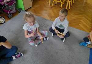 Dziewczynka i chłopiec wystukują rytm na pałeczkach.