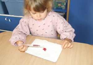 Dziewczynka nalewa tusz pipetą na wacik.