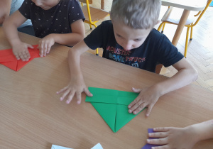 Dzieci składają przy stole łódkę z papieru techniką origami.