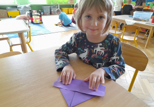 Dziewczynka składa przy stole łódkę z papieru techniką origami.